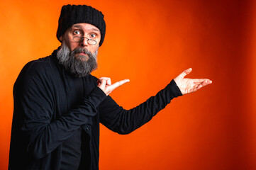 Expressive man with beard and glasses points with both hands on vibrant orange background....