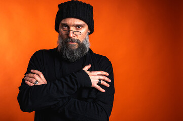 Confident man with beard, glasses, and beanie, arms crossed. Unwavering gaze in studio portrait on...