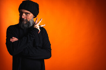 Confident man with beard, glasses, and beanie, arms crossed. Unwavering gaze in studio portrait on...