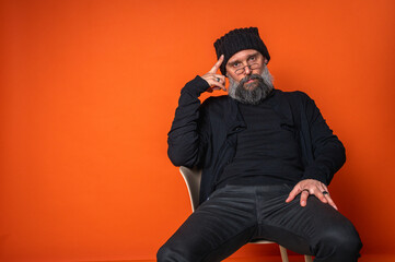 Expressive man with beard, glasses, and beanie, hand to temple. Deep in thought in studio portrait...