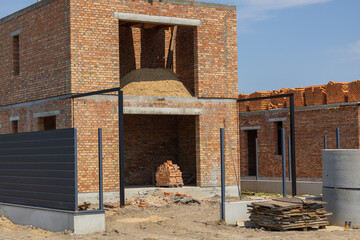 New brick buildings are under construction with sand piles and building materials scattered around...