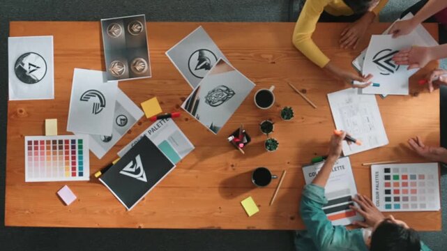 Top view of designer writing and designing logo graphic at meeting. Closeup of business man working on colored palettes and writing idea on sticky notes on table with equipment and paper. Symposium.