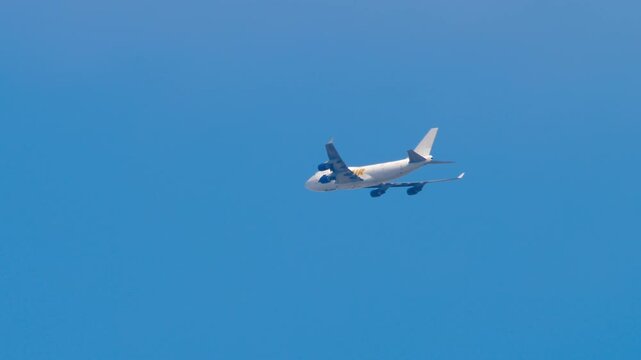 Heavy wide-body four-engine jumbo jet aircraft in the blue sky, long shot