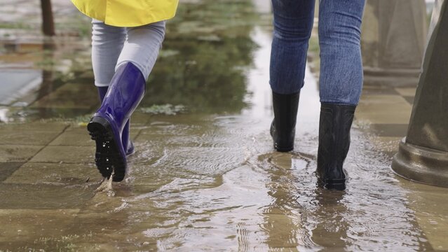 people walk through puddles in rubber boots, heavy rainfall on asphalt, splashing puddles flying in different directions, lot of water flooding the road, the city's climatic changes, the environment. - Powered by Adobe