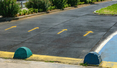 High angle shot of an outdoor asphalt pathway marked with several yellow arrows pointing forward. Park is bordered by green bushes and curbs. Symbolizing for movement or decision-making.