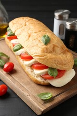Tasty sandwich with mozzarella cheese, tomatoes and basil on black wooden table, closeup