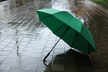 Green umbrella on wet asphalt outdoors, space for text