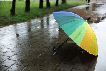 Colorful umbrella on wet asphalt outdoors, space for text