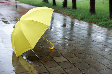 Yellow umbrella on wet asphalt outdoors, space for text