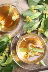 Tasty linden tea in cups, leaves and flowers on wooden table, flat lay
