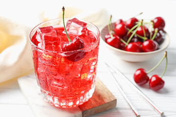 Tasty cherry soda with ice cubes and berries in glass on white wooden table, closeup