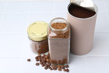 Instant coffee in jars and beans on white tiled table, closeup