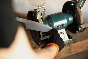 Man sharpening knife with bench grinder indoors, closeup