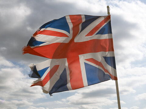 tattered British national union flag flying against a cloudy sky