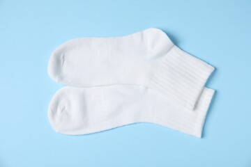 Pair of comfortable white socks on light blue background, top view