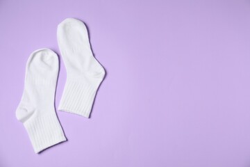 Pair of comfortable white socks on violet background, top view. Space for text