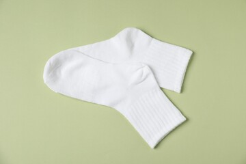 Pair of comfortable white socks on light green background, top view