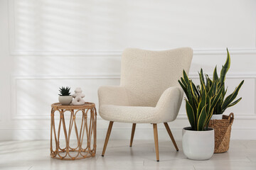 Comfortable armchair, side table and houseplants near white wall indoors