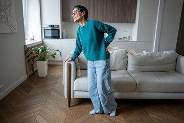 Mature woman hunched over in discomfort attempting to stand from sofa. Sciatica pain, slipped disc,...