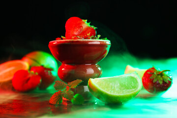 Hookah bowl with limes, strawberries, mint and smoke on black table, closeup
