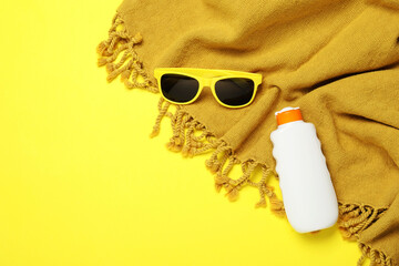 Beach towel, sunglasses and sunscreen on yellow background, flat lay. Space for text