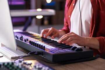 Man working with MIDI keyboard at wooden table indoors, closeup