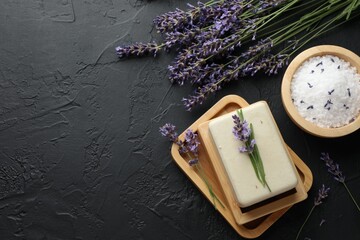 Obraz na płótnie Canvas Aromatic soap bar, sea salt and lavender flowers on dark textured table, flat lay. Space for text