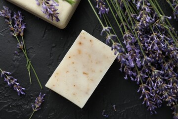 Aromatic soap bars and lavender flowers on dark textured table, flat lay