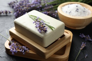 Aromatic soap bar and lavender flowers on dark textured table, closeup