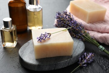 Aromatic soap bar and lavender flowers on dark textured table, closeup