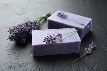 Aromatic soap bars and lavender flowers on dark textured table, closeup