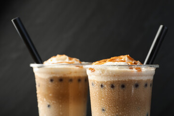 Tasty milk bubble tea in plastic cups on black background, closeup