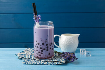 Tasty milk bubble tea in glass and lavender flowers on light blue wooden table
