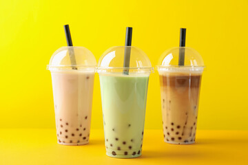 Tasty milk bubble tea in plastic cups on yellow background