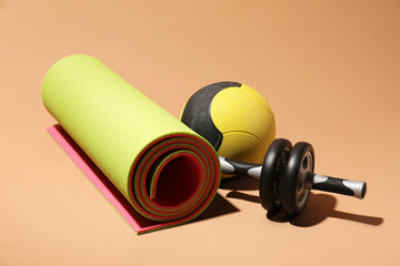 Medicine ball, fitness mat and ab wheel on beige background