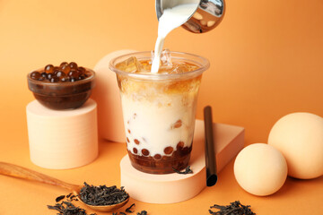 Pouring milk into bubble tea on orange background, closeup