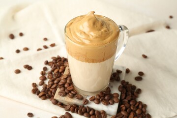 Delicious dalgona coffee in glass cup and beans on table, closeup