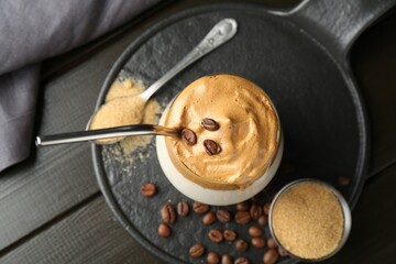 Delicious dalgona coffee in glass, beans and brown sugar on wooden table, top view
