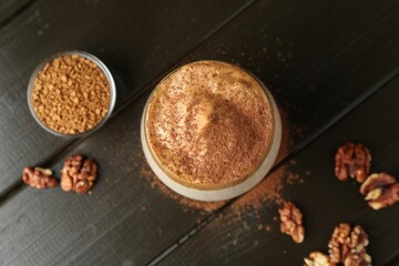 Delicious dalgona coffee in glass, granules, walnuts and brown sugar on wooden table, flat lay