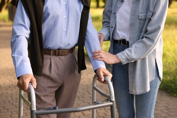 Caregiver supporting elderly man who using walking frame outdoors, closeup