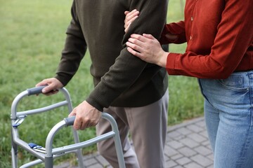 Caregiver supporting elderly man who using walking frame outdoors, closeup