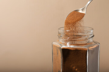 Taking instant coffee with spoon on beige background, closeup. Space for text