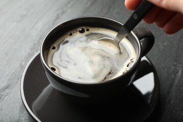Woman stirring instant coffee with spoon at black table, closeup
