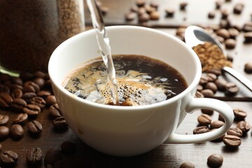 Pouring hot water into cup with instant coffee at wooden table, closeup