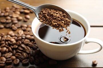 Putting instant coffee into cup of hot drink at wooden table, closeup