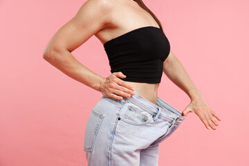 Fit woman wearing old jeans after weight loss on pink background, closeup