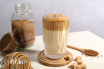 Delicious dalgona coffee in glass, whisk, brown sugar and granules on light table
