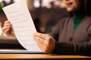 Mature student reviews paperwork for her degree in a classic library setting, using multiple...