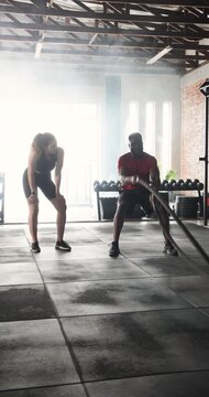 Vertical video: Trainer starting rope waves, guiding client through strength workout in gym