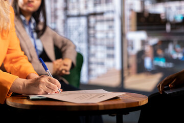Multicultural team of female leaders in a corporate meeting sign an agreement, collaborating for...